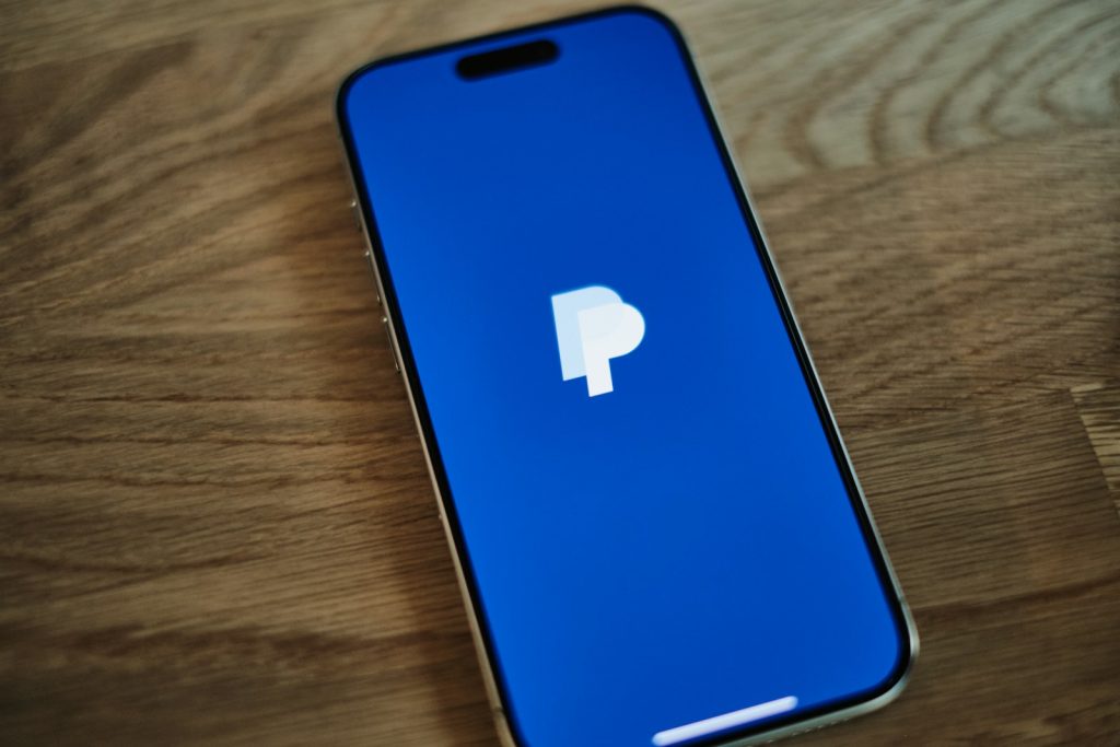 Ein blaues iPhone, das auf einem Holztisch liegt und PayPal geöffnet hat