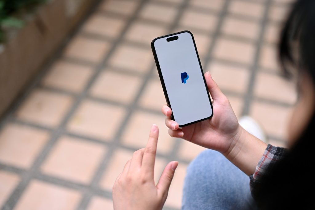 Frau hält Handy in der Hand. Geöffnet ist PayPal