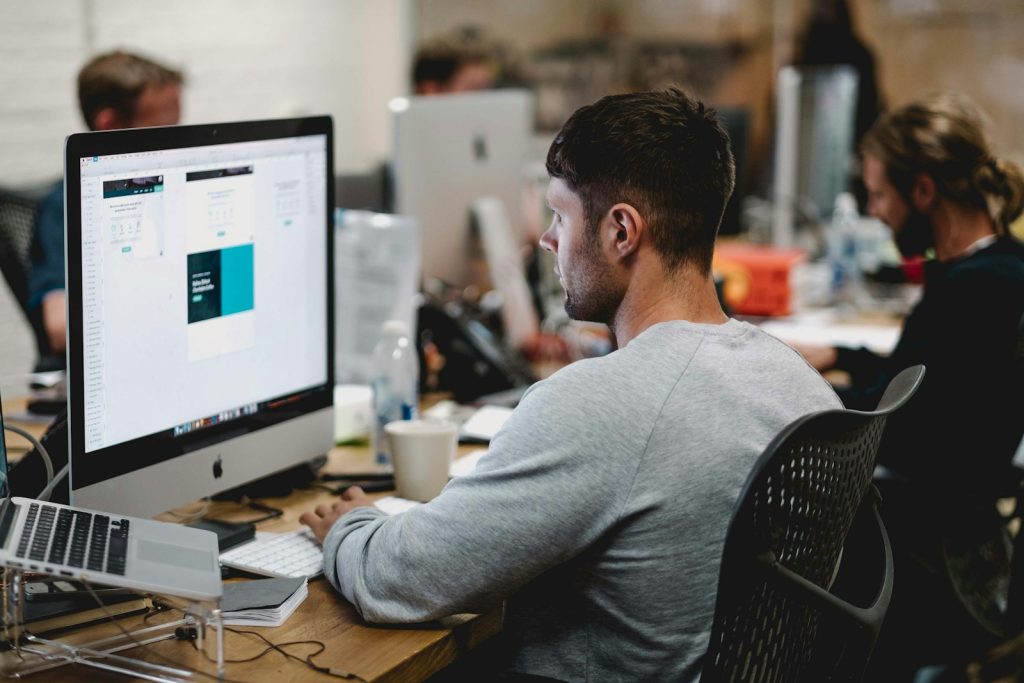 Mann in grauem Sweatshirt sitzt auf einem Stuhl vor einem iMac