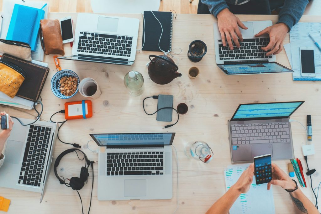Menschen, die sich an einen Tisch mit verschiedenen Laptops setzen und eine positive Unternehmenskultur repräsentieren