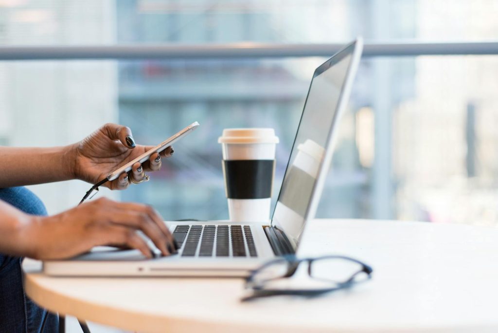 Nahaufnahme von Händen mit einem Laptop und einem Telefon mit Kaffee auf einem modernen Büroschreibtisch.