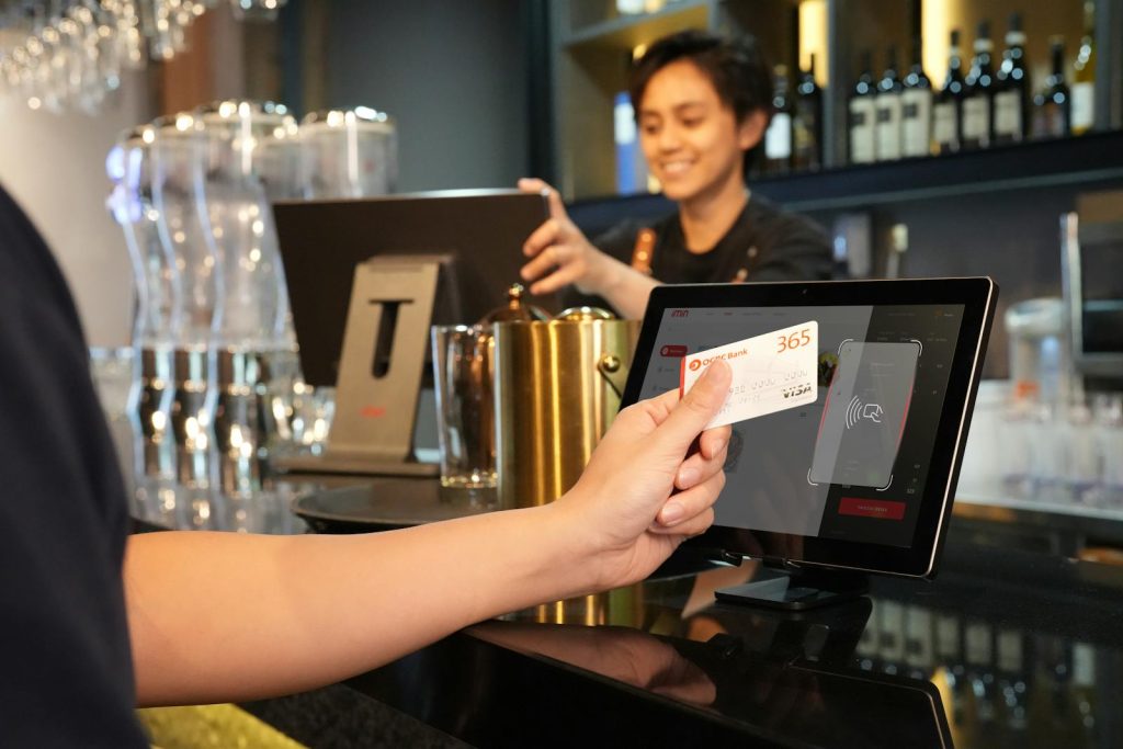 
Person, die in einer modernen Bar kontaktloses Bezahlen mit Kreditkarte nutzt, unterstützt von einem Kassierer.