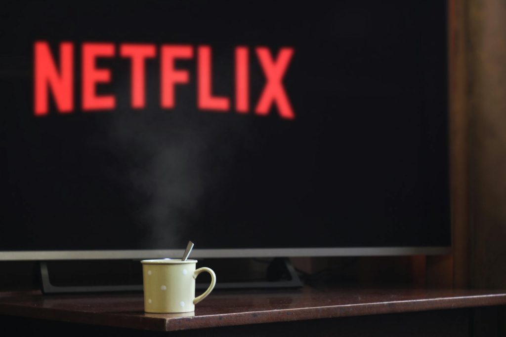 Eine dampfende Tasse auf einem Tisch vor einem Fernseher mit Netflix, der eine gemütliche Innenatmosphäre schafft.