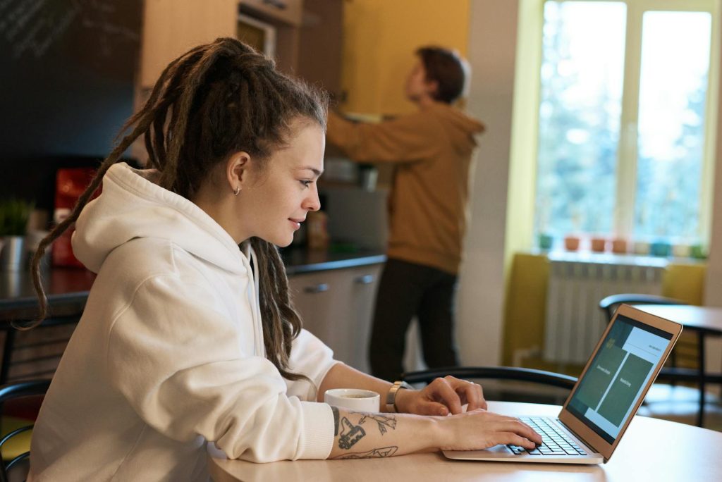 Junge Frau mit Dreadlocks arbeitet in ungezwungener Küchenumgebung an einem Laptop.