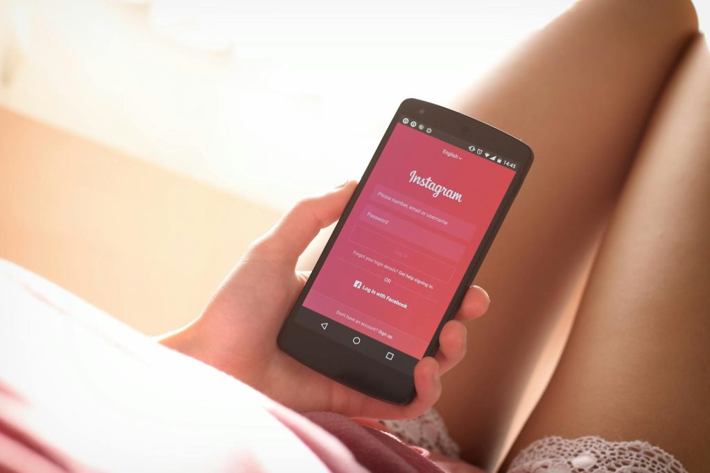 Frau hält ein Smartphone mit Instagram-Anmeldebildschirm in der Hand, während sie sich drinnen entspannt.