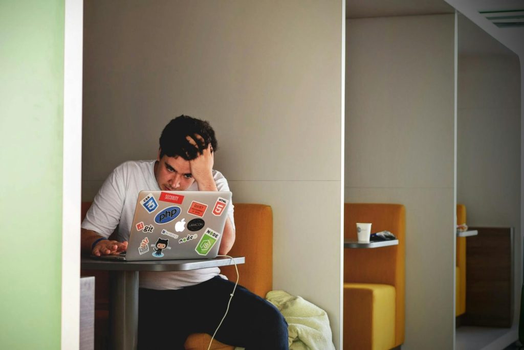 Mann zeigt Stress und Frustration, während er drinnen an einem Laptop arbeitet.