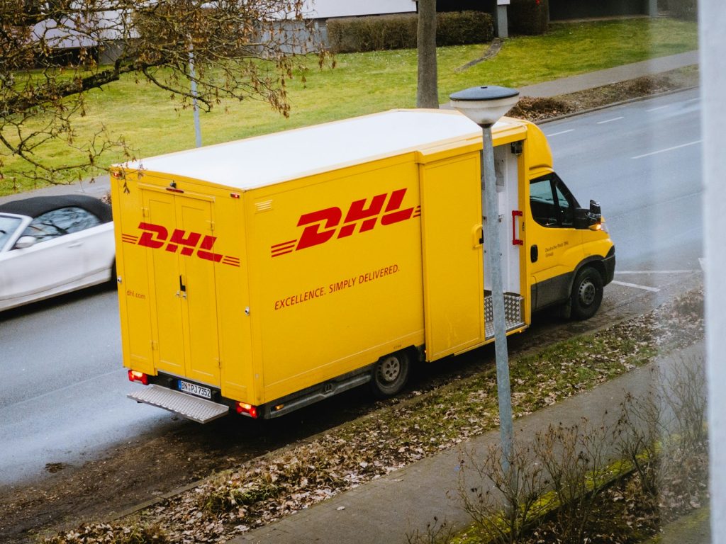 Weißer und orangefarbener Kastenwagen, der tagsüber in der Nähe kahler Bäume geparkt ist.