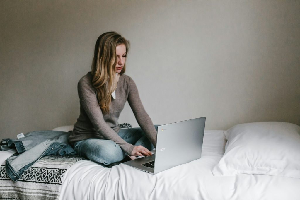 Frau tippt auf dem windows Laptop, während sie im Zimmer auf dem Bett sitzt