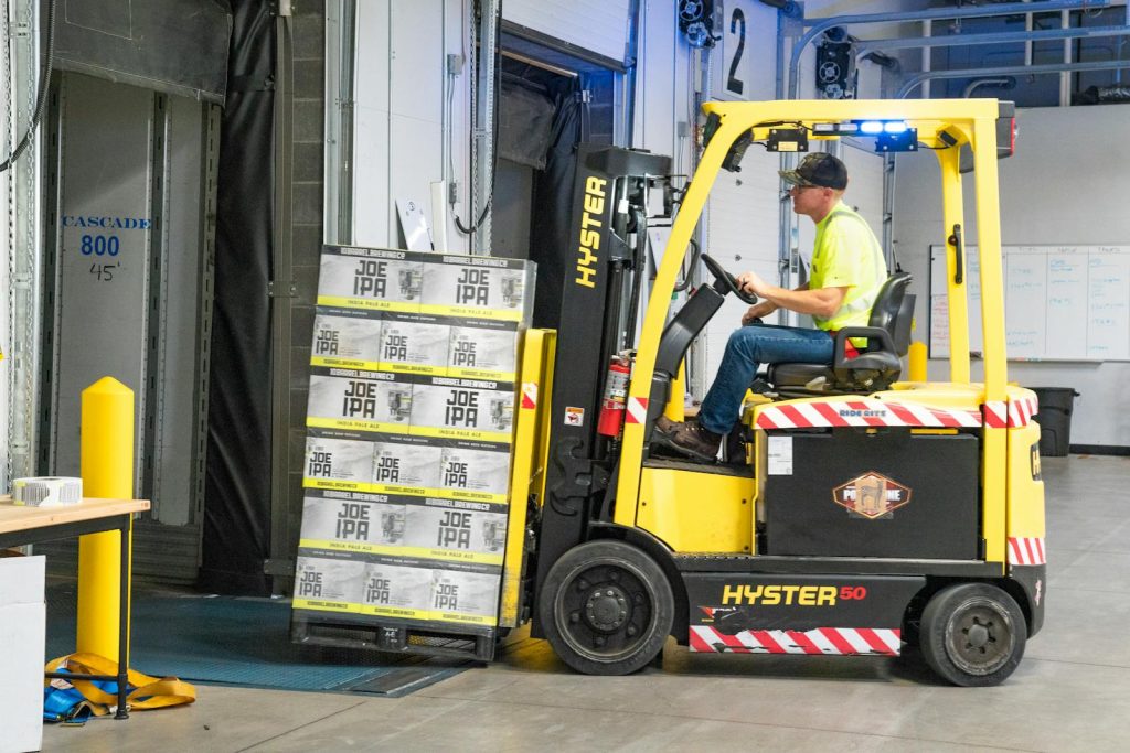 Ein Arbeiter fährt einen Hyster-Gabelstapler und bewegt Joe-IPA-Kisten in einem Lager.